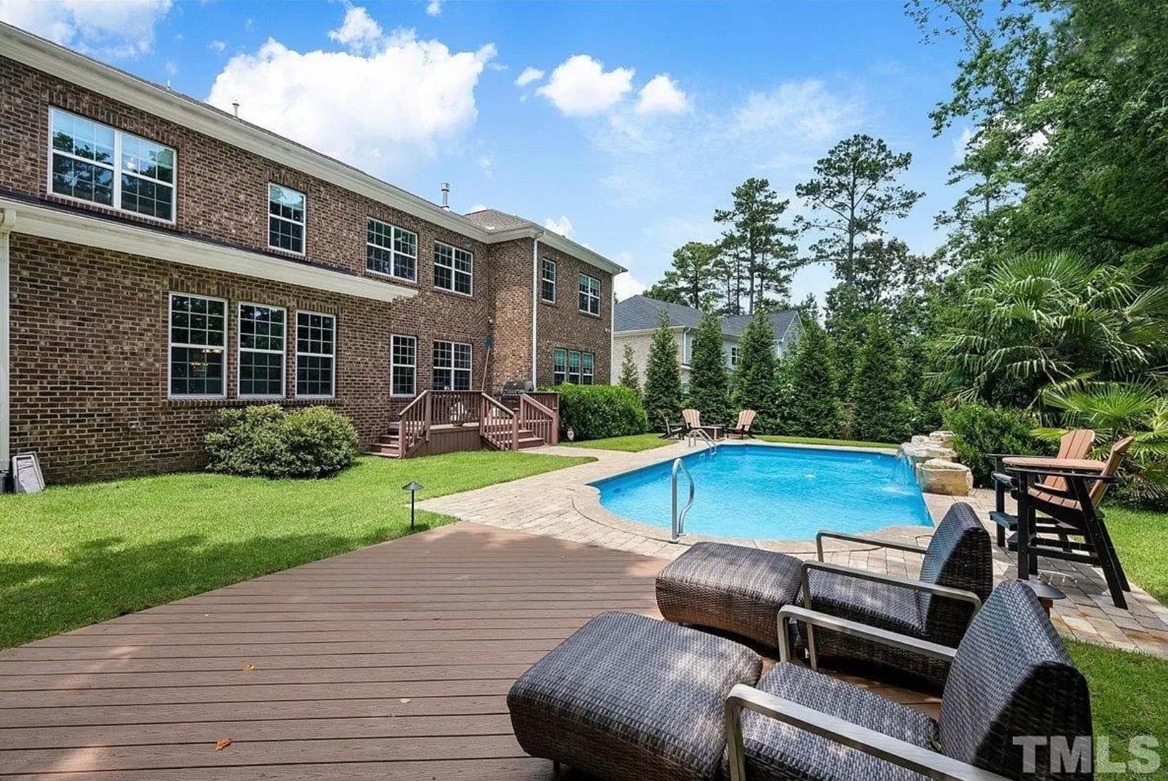 A two-story brick home with a back porch, large yard with a bright blue pool, deck area, and mature landscaping